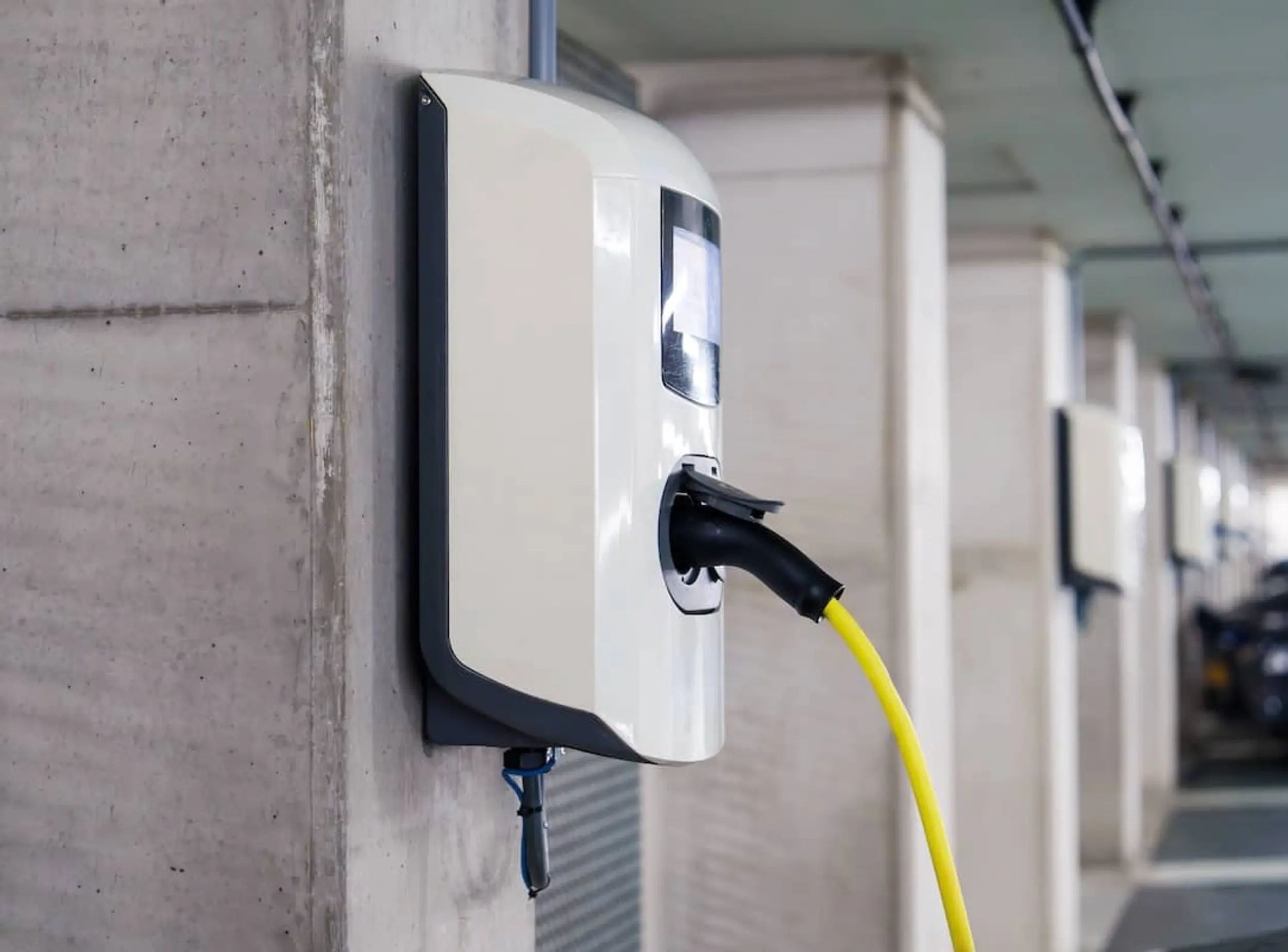 EV-Ladestation mit einem angeschlossenen gelben Kabel in einem Parkhaus.