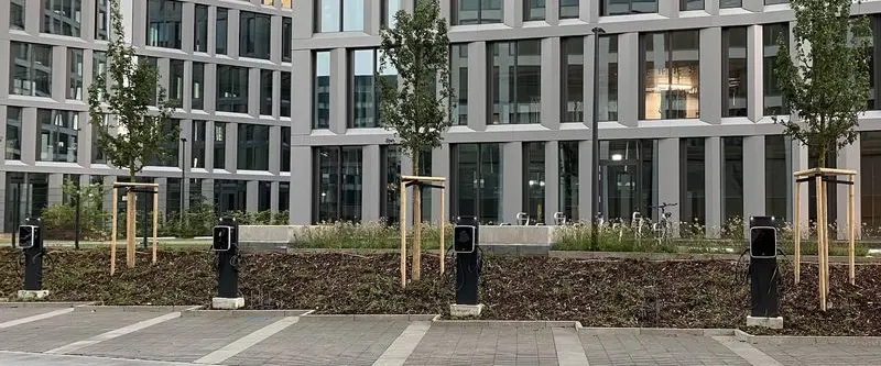 Bürogebäude mit Bäumen und Ladesäulen im Vordergrund