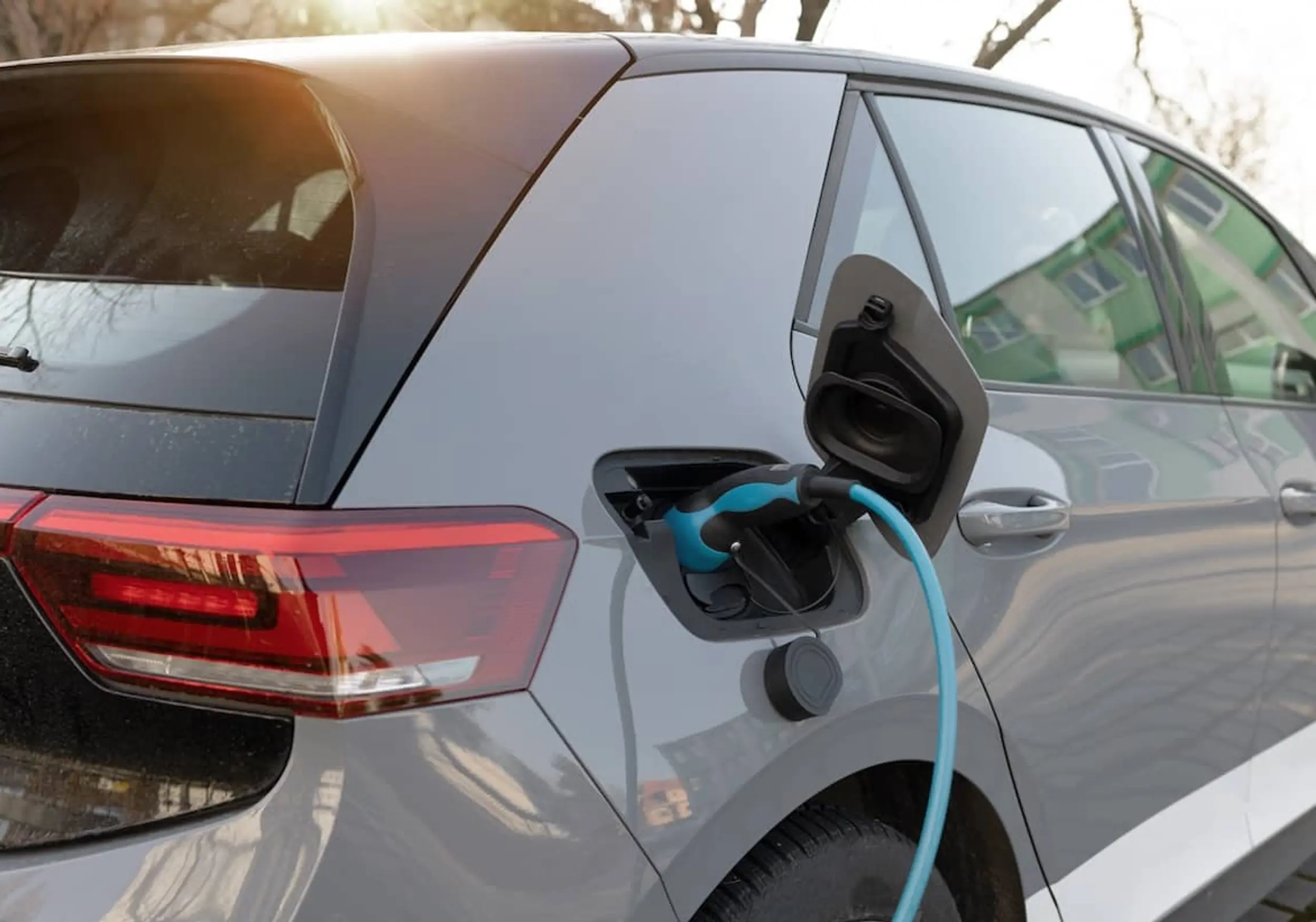 Ein graues Elektroauto wird mit einem blauen Kabel geladen, das in seinen offenen Anschluss eingesteckt ist.