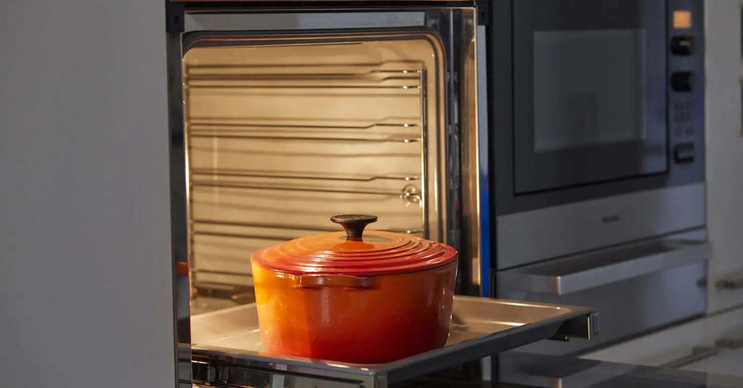 Orangener Le Creuset Topf auf Backblech bei geöffnetem Ofen