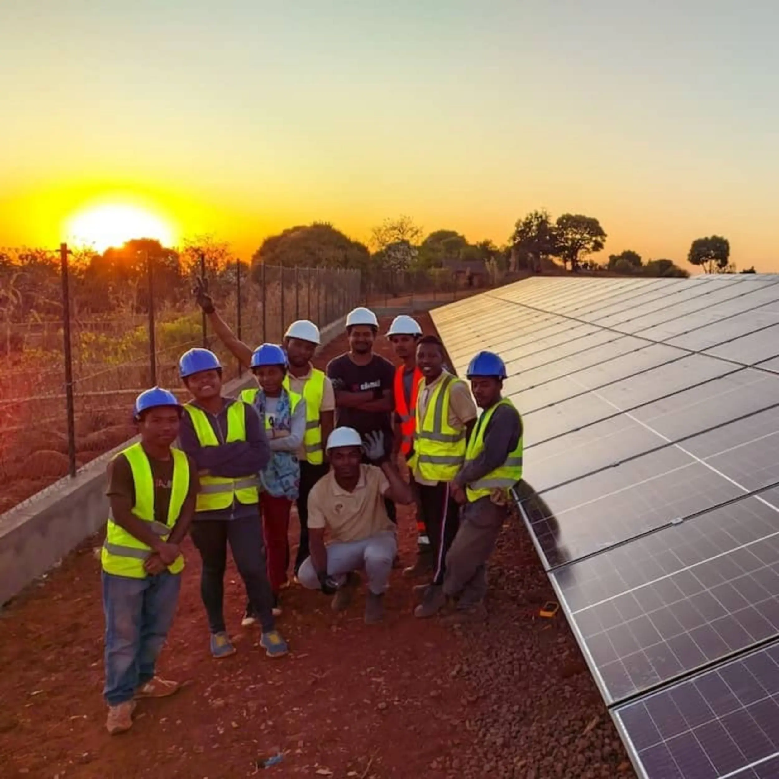 Mitarbeiter von AfricaGreenTec stehen mit gelber Weste und Helm bei Sonnenuntergang neben einer Photovoltaikanlage in Madagaskar