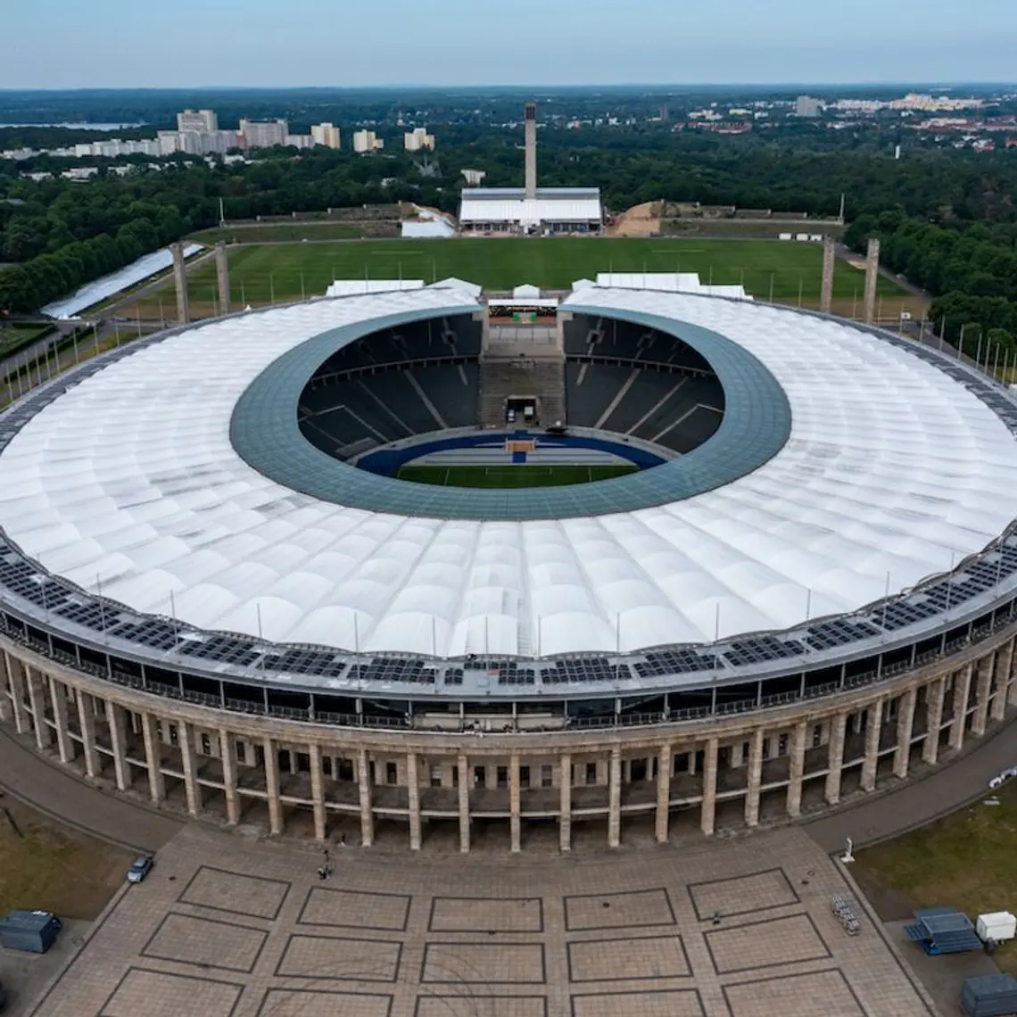 Blick von einer Drohne seitlich auf das Berliner Olympiastadion mit Photovoltaikanlage ringsum das weiße Stadiondach