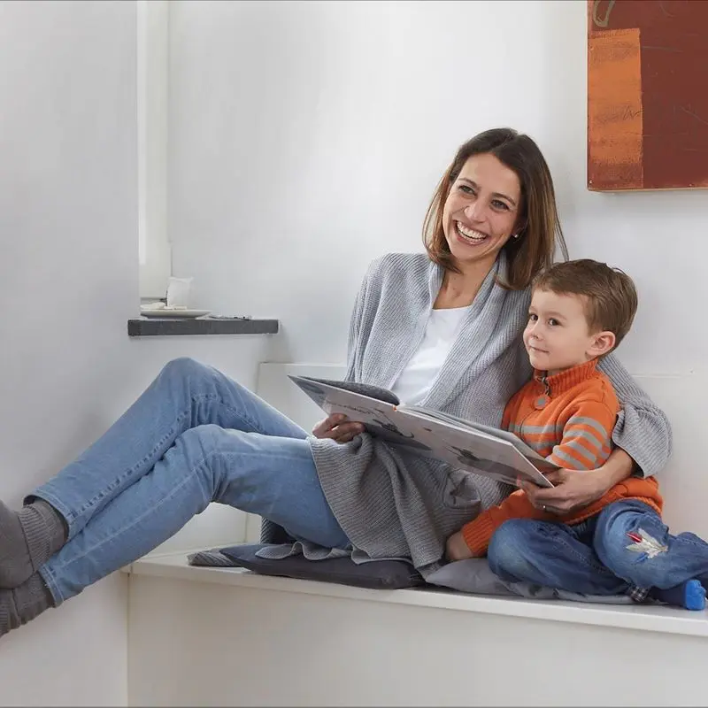 Eine Frau wärmt sich die Füße an einer Heizung und liest einem Kind ein Buch vor