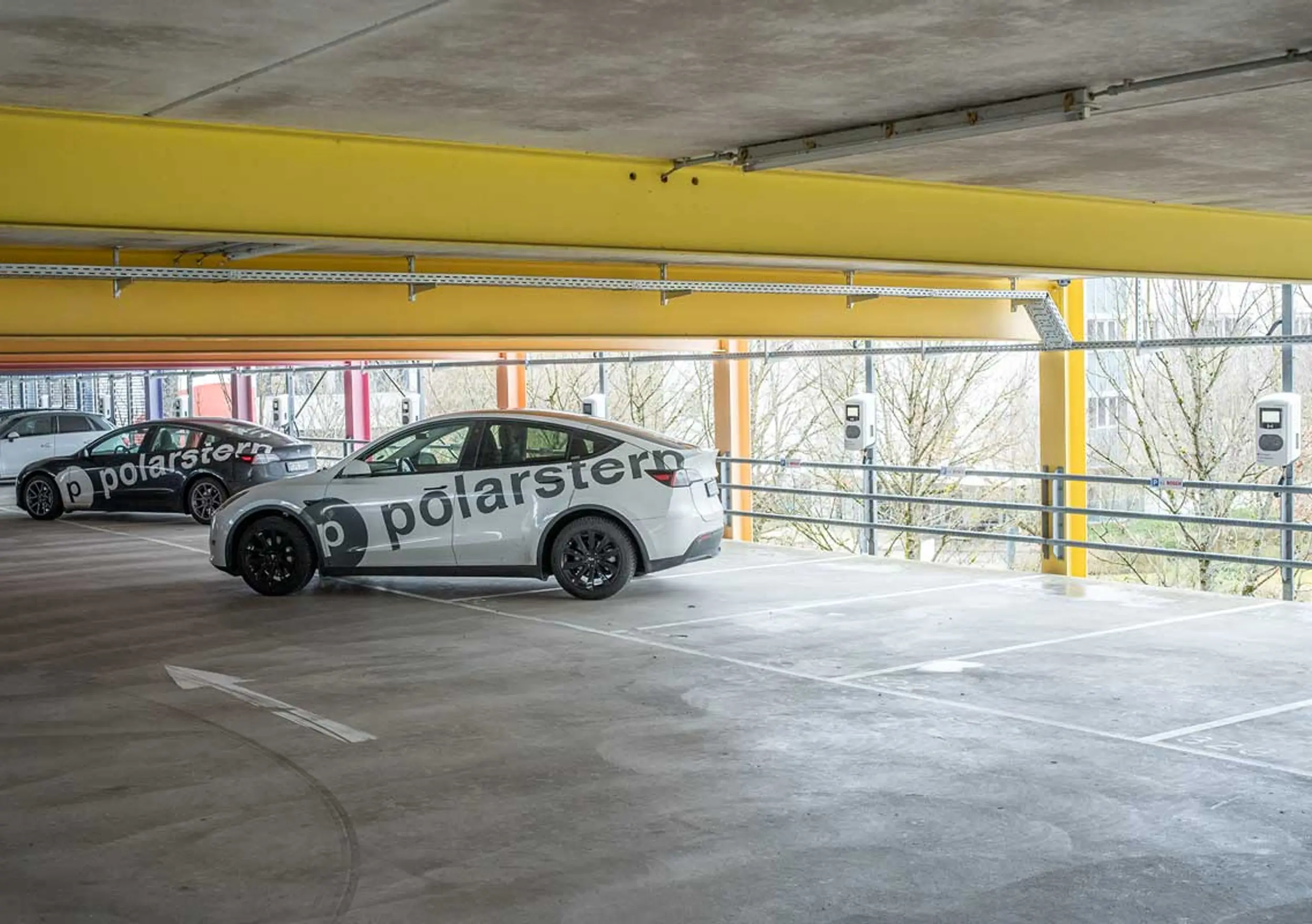 Zwei Autos, ein weißes und ein schwarzes, mit der Marke „polarstern“, in einer Parkgarage mit Ladestationen für Elektrofahrzeuge.