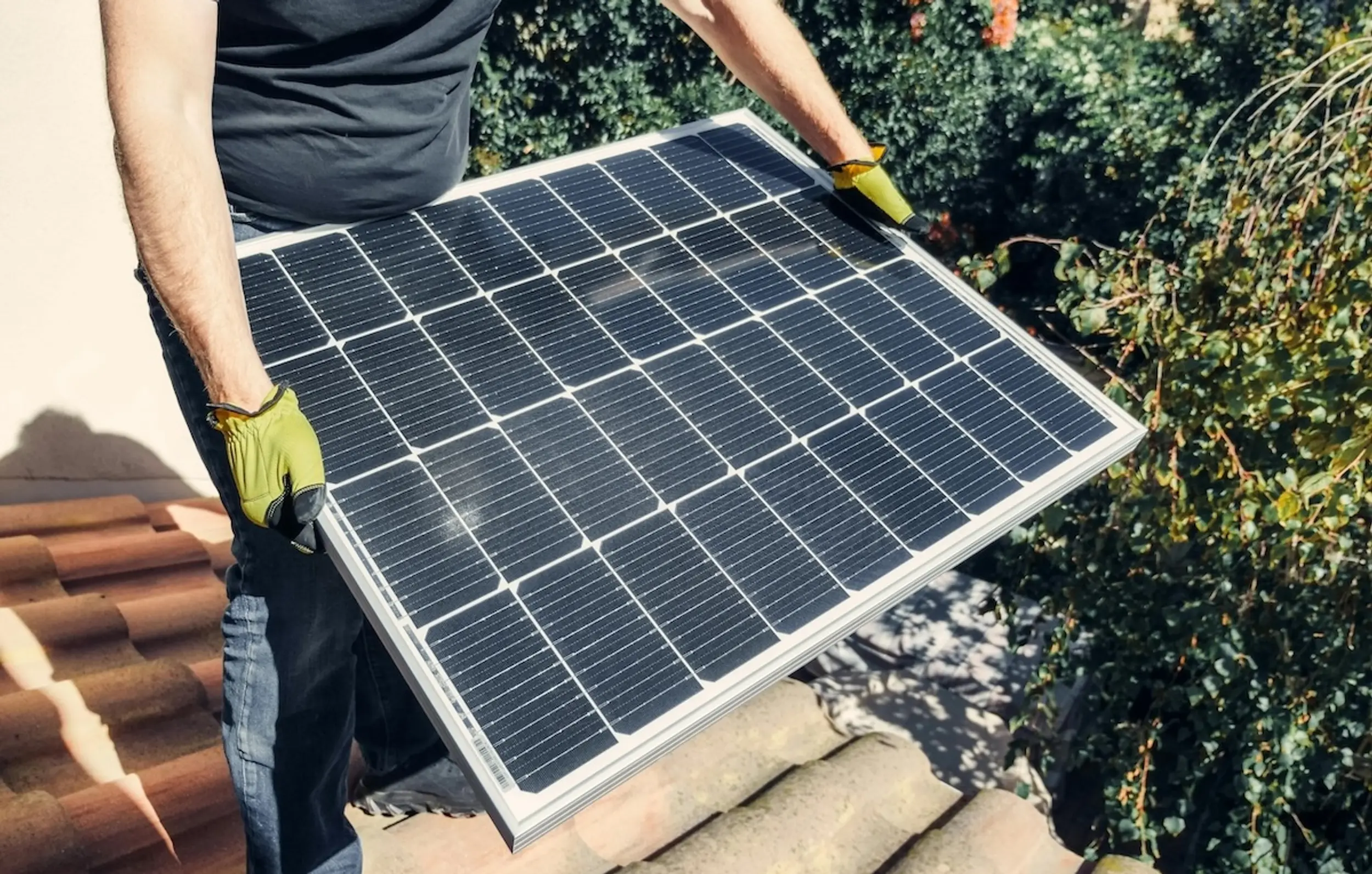 Mann hält PV-Modul auf Ziegeldach