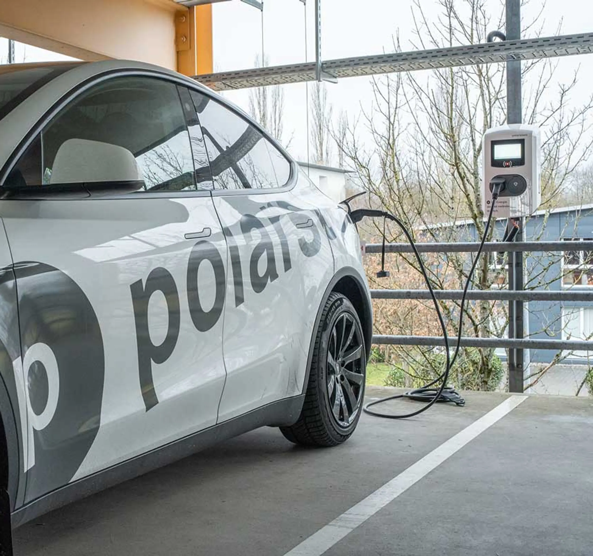 Ein weißes Elektroauto mit der Aufschrift „polars“ lädt an einer Ladestation für Elektrofahrzeuge auf einem Parkplatz.