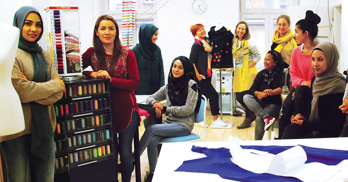 Stich by Stich: Eine Gruppe von Schneiderinnen steht nebeneinander in einem Raum.