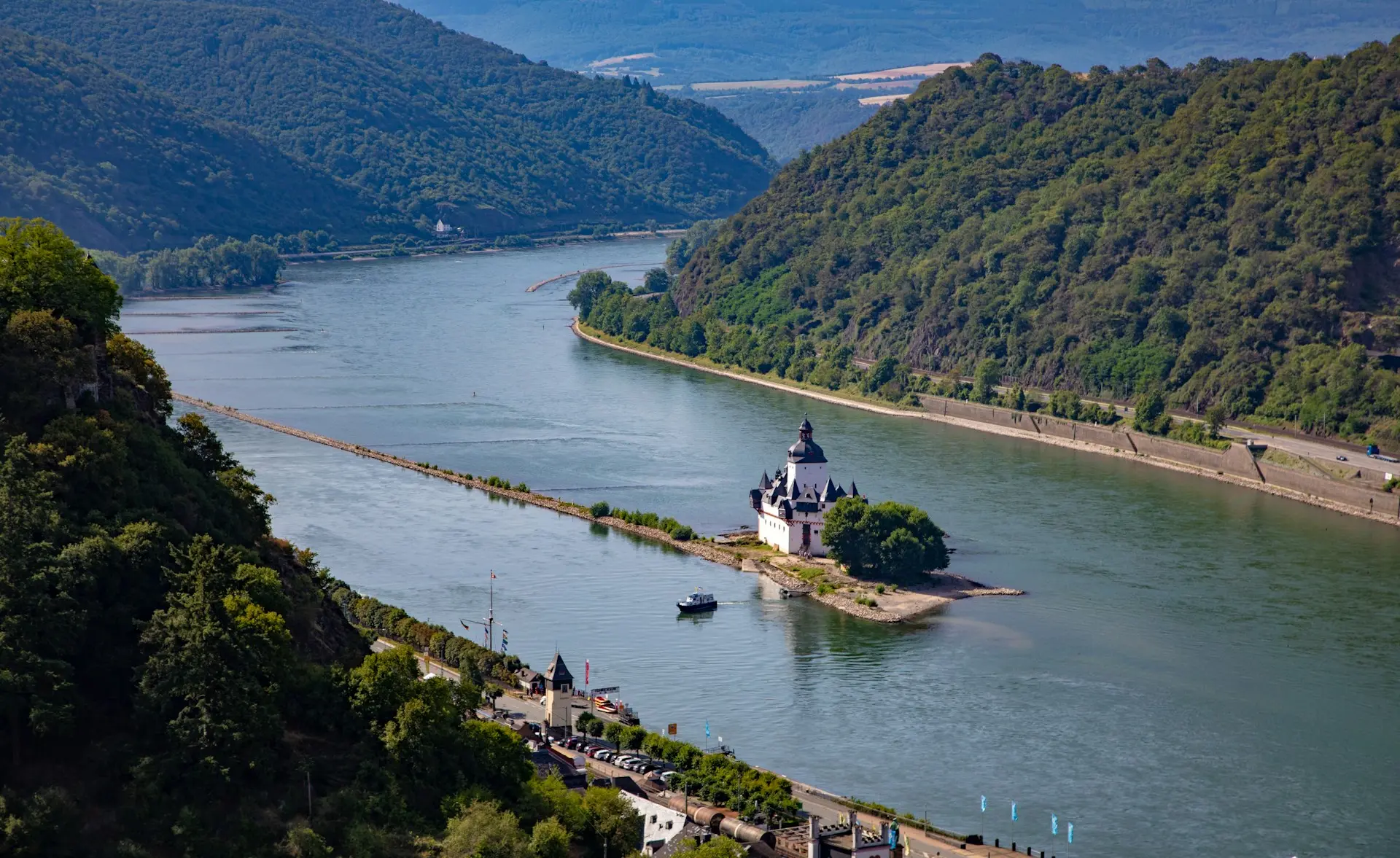 Quelle: Unsplash/Katja Ano A river winds through a valley of forested hills, with a white castle on a small island in the middle of the river.