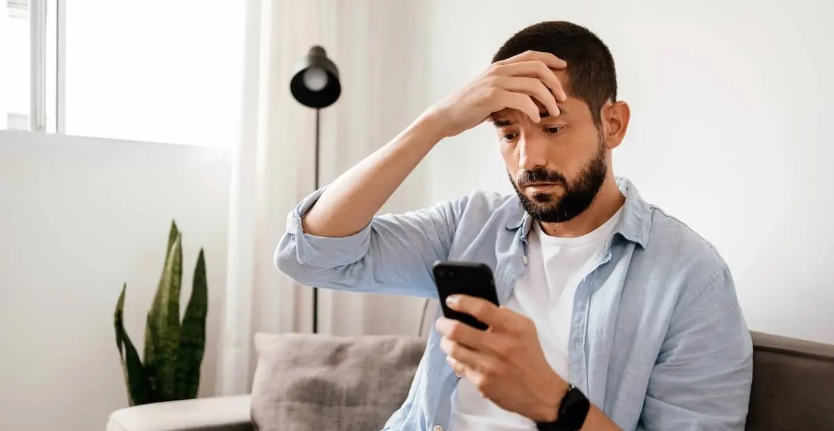 Ein Mann sieht besorgt aus, während er sein Smartphone hält und darauf schaut, mit einer Hand an seiner Stirn.