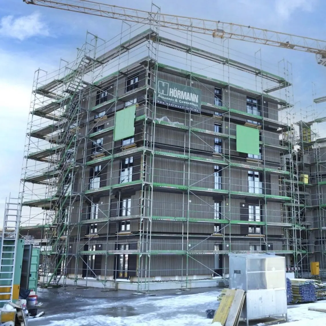 Rohbau von mehrstöckigem Wohngebäude mit Baugerüst drumherum und einem Kran im Winter
