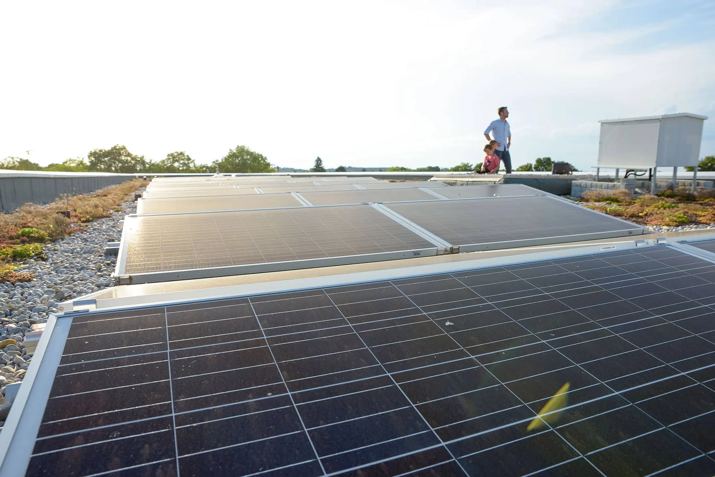 Bild zeigt Photovoltaikanlagen auf einem Mehrparteiengebäude, und im Hintergrund stehen ein Mann, der in die Ferne schaut, und seine Kinder.