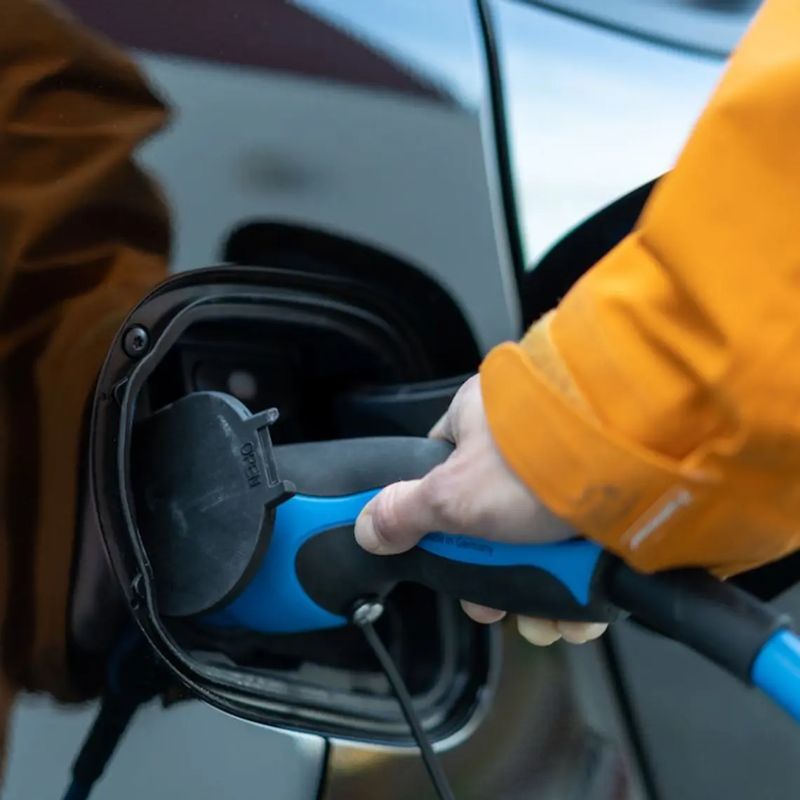 Eine Hand steckt ein Ladekabel in den Tank eines E-Autos