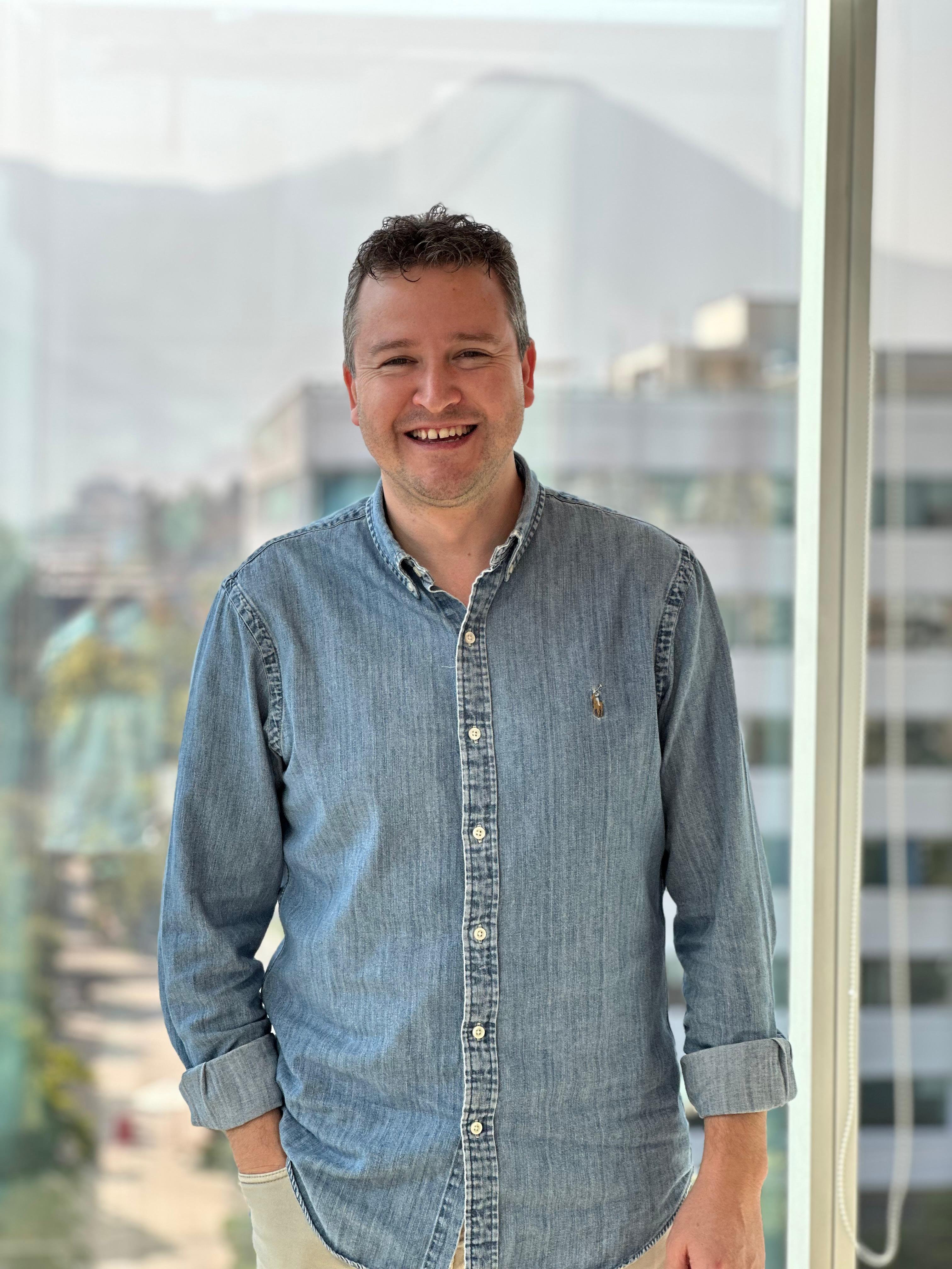 a man in a denim shirt is smiling in front of a window
