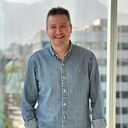a man in a denim shirt is smiling in front of a window