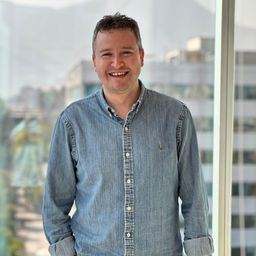 a man in a denim shirt is smiling in front of a window