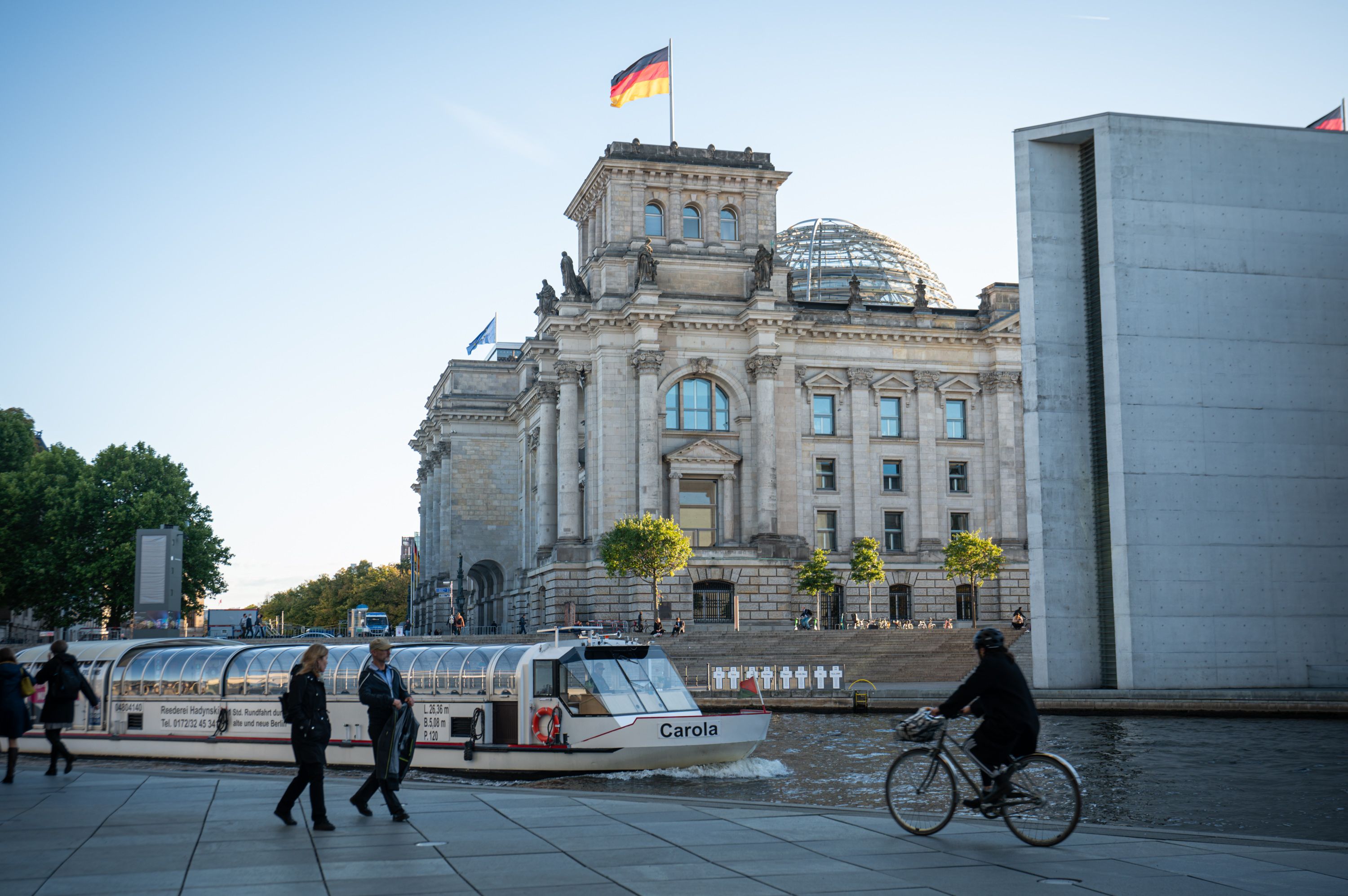 A boat floats along in the river of the governmental district with the German Parliament in the background.