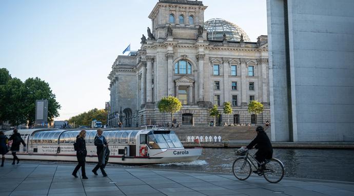 A boat floats along in the river of the governmental district with the German Parliament in the background.