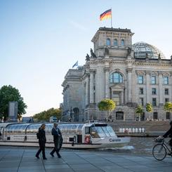 A boat floats along in the river of the governmental district with the German Parliament in the background.