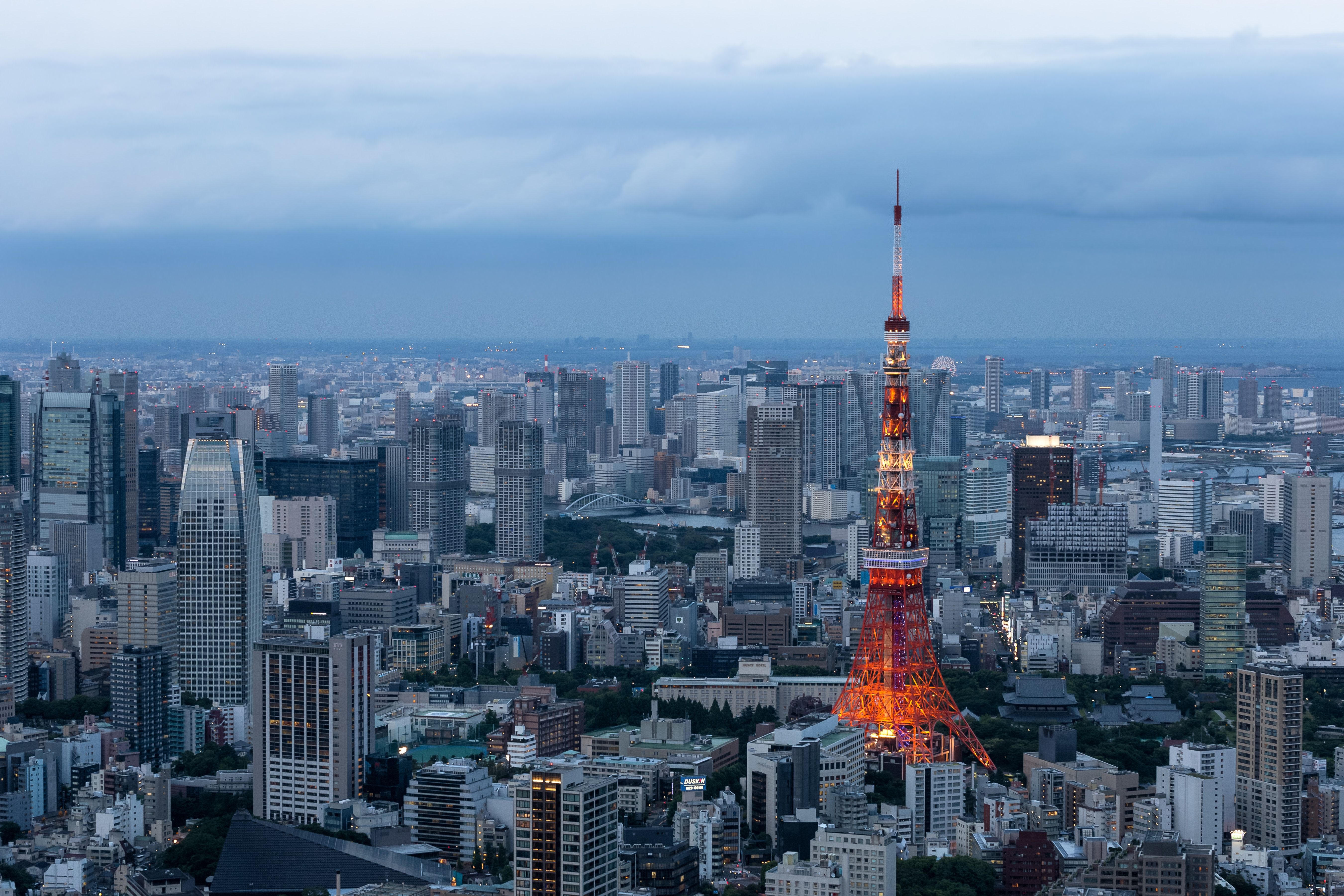 Tokyo tower is illuminated at dusk against a skyline of tall buildings