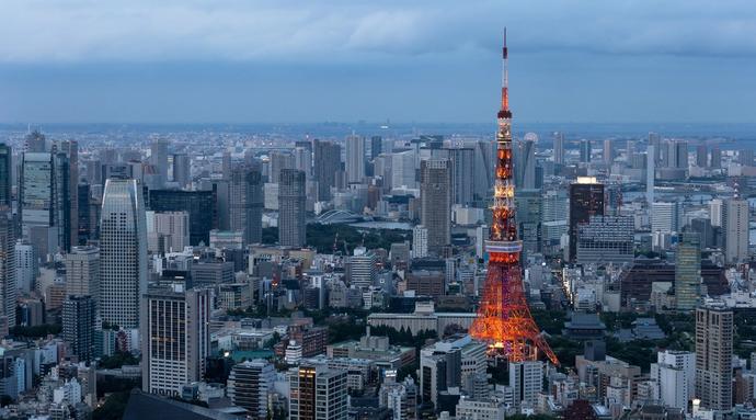 Tokyo tower is illuminated at dusk against a skyline of tall buildings