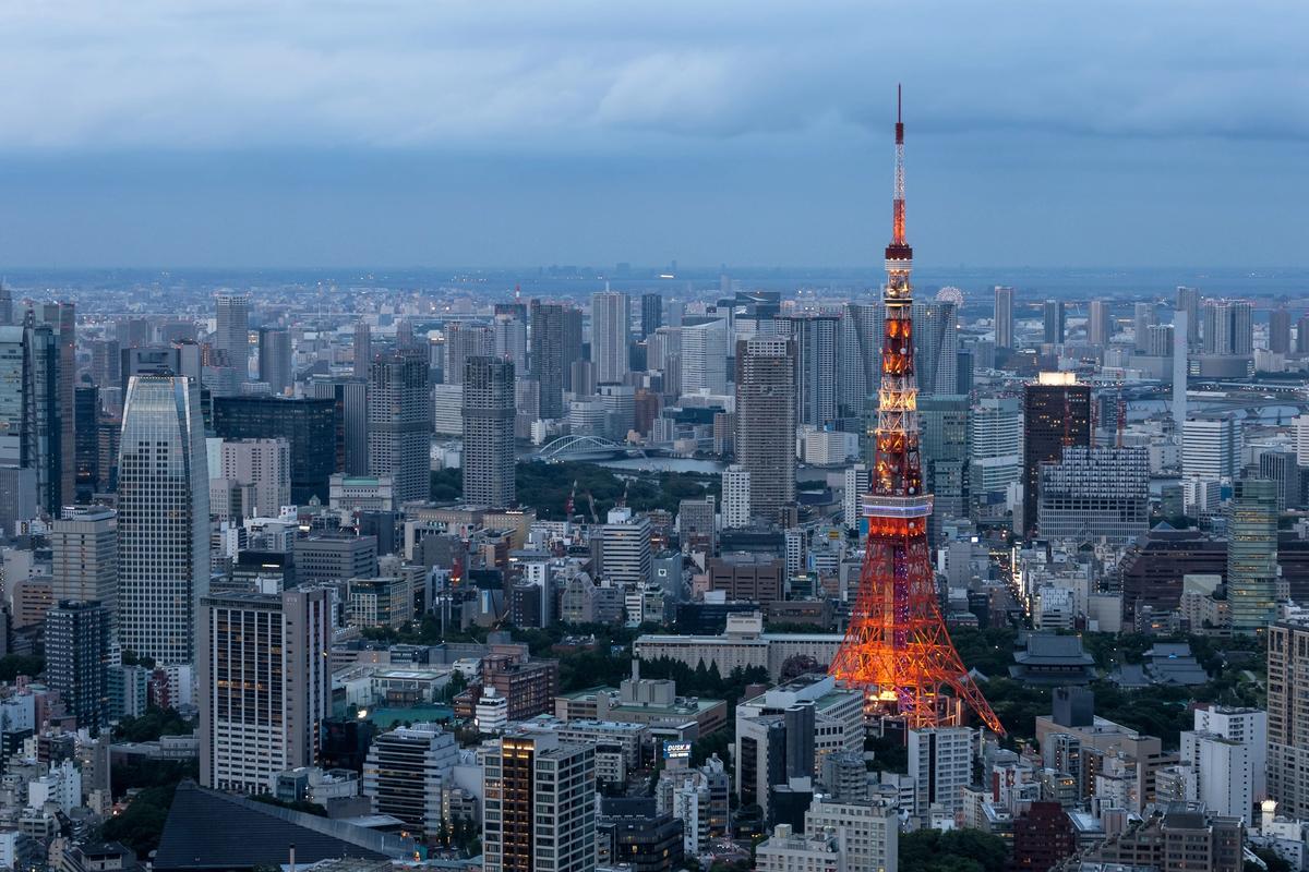 Tokyo tower is illuminated at dusk against a skyline of tall buildings