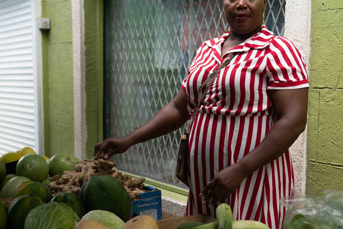 A woman stands outside behind a fruit and produce stand
