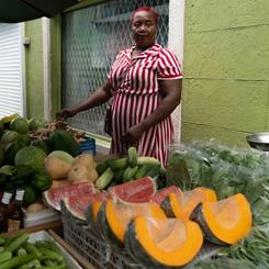 A woman stands outside behind a fruit and produce stand