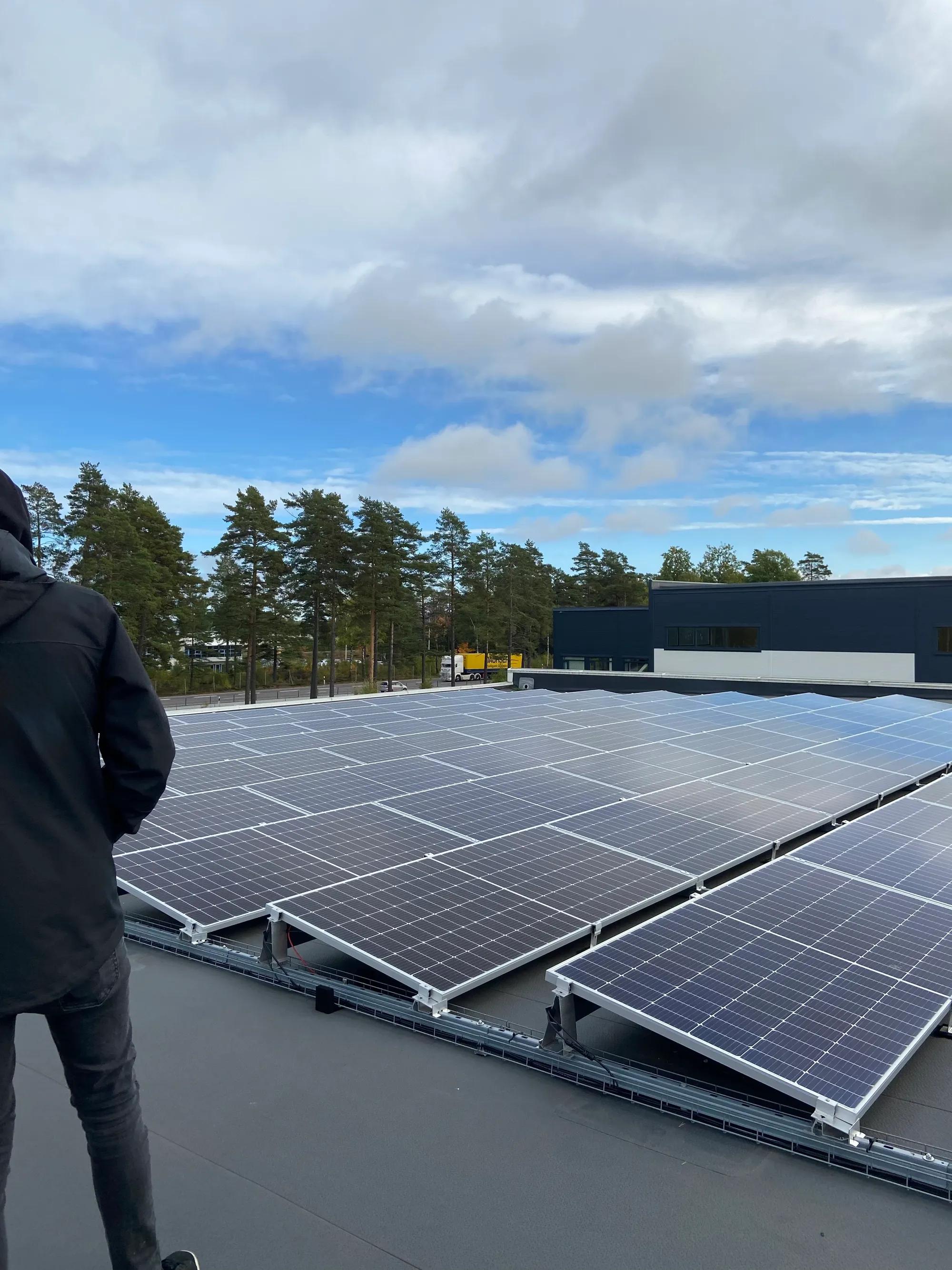 Montör på det platta taket bredvid vinklade solpaneler, med tallar i bakgrunden