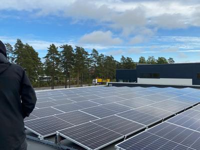 Montör på det platta taket bredvid vinklade solpaneler, med tallar i bakgrunden