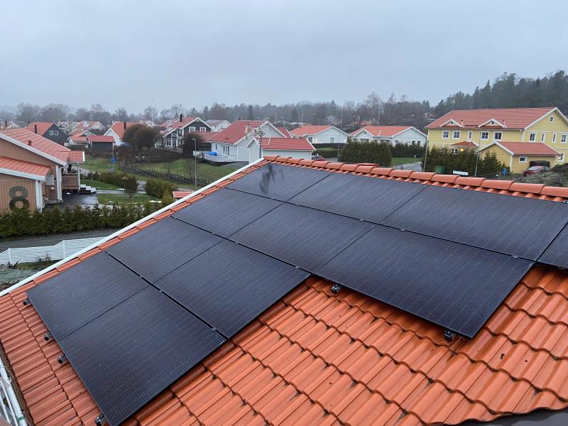 Helsvarta solpaneler på ett rött tegeltak i ett villaområde