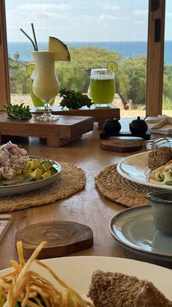 Platos de comida y dos bebidas tropicales sobre una mesa de madera con vistas al Pacífico.