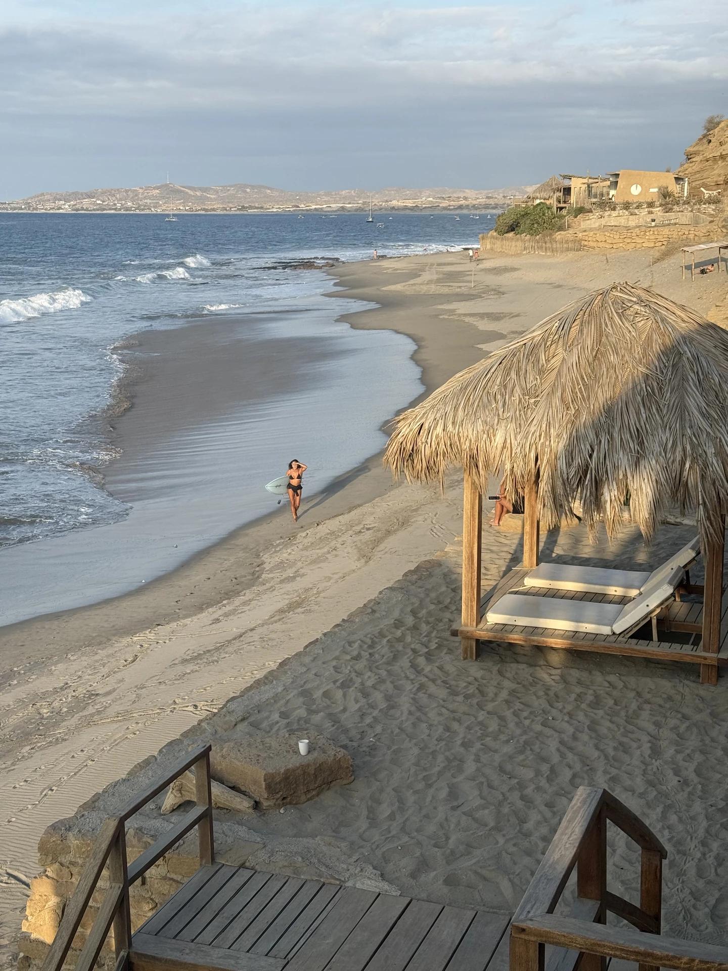 Vista de la bahía con olas, refugios de playa y embarcaciones mar adentro.