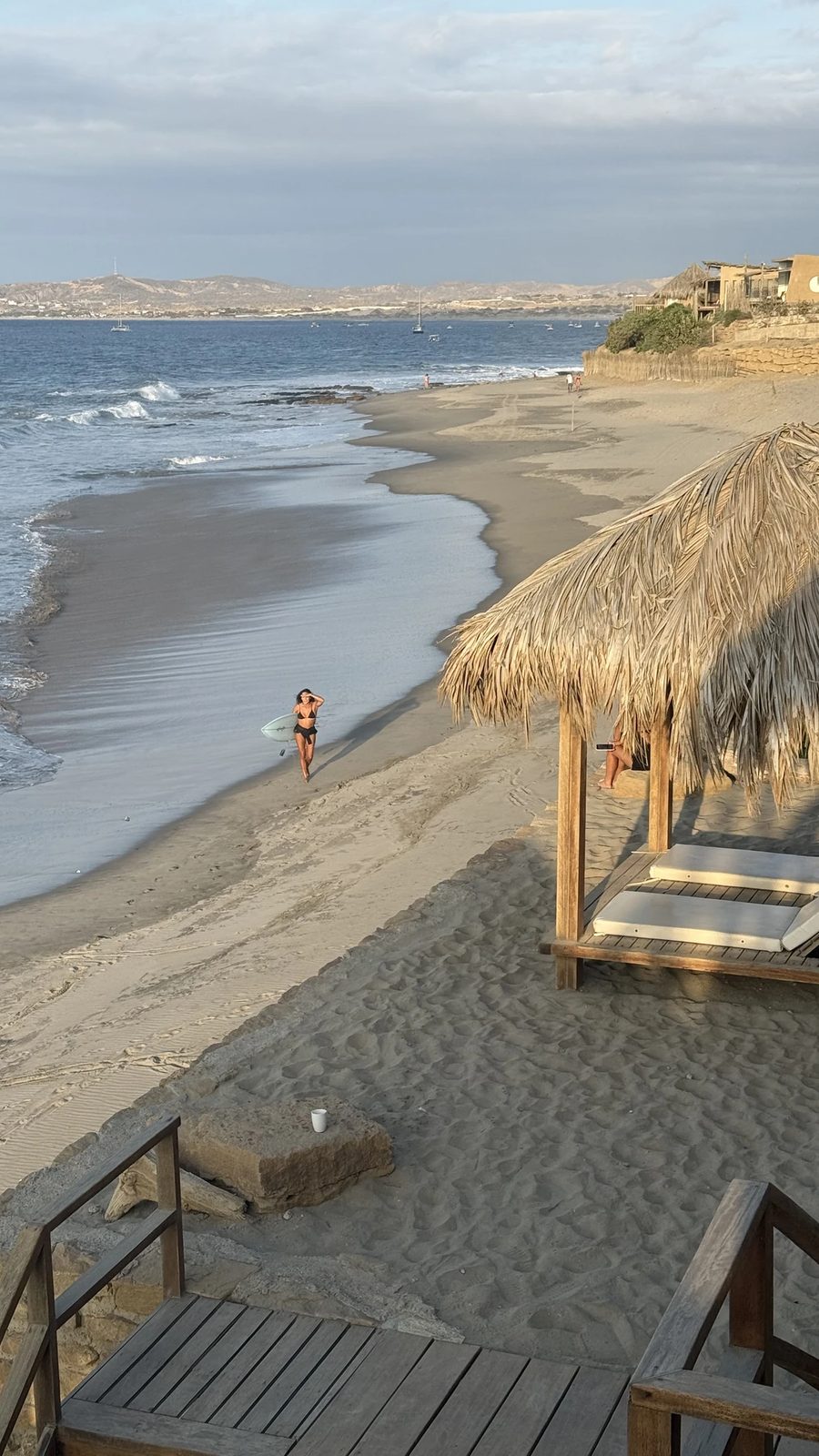 Vista de la bahía con olas, refugios de playa y embarcaciones mar adentro.