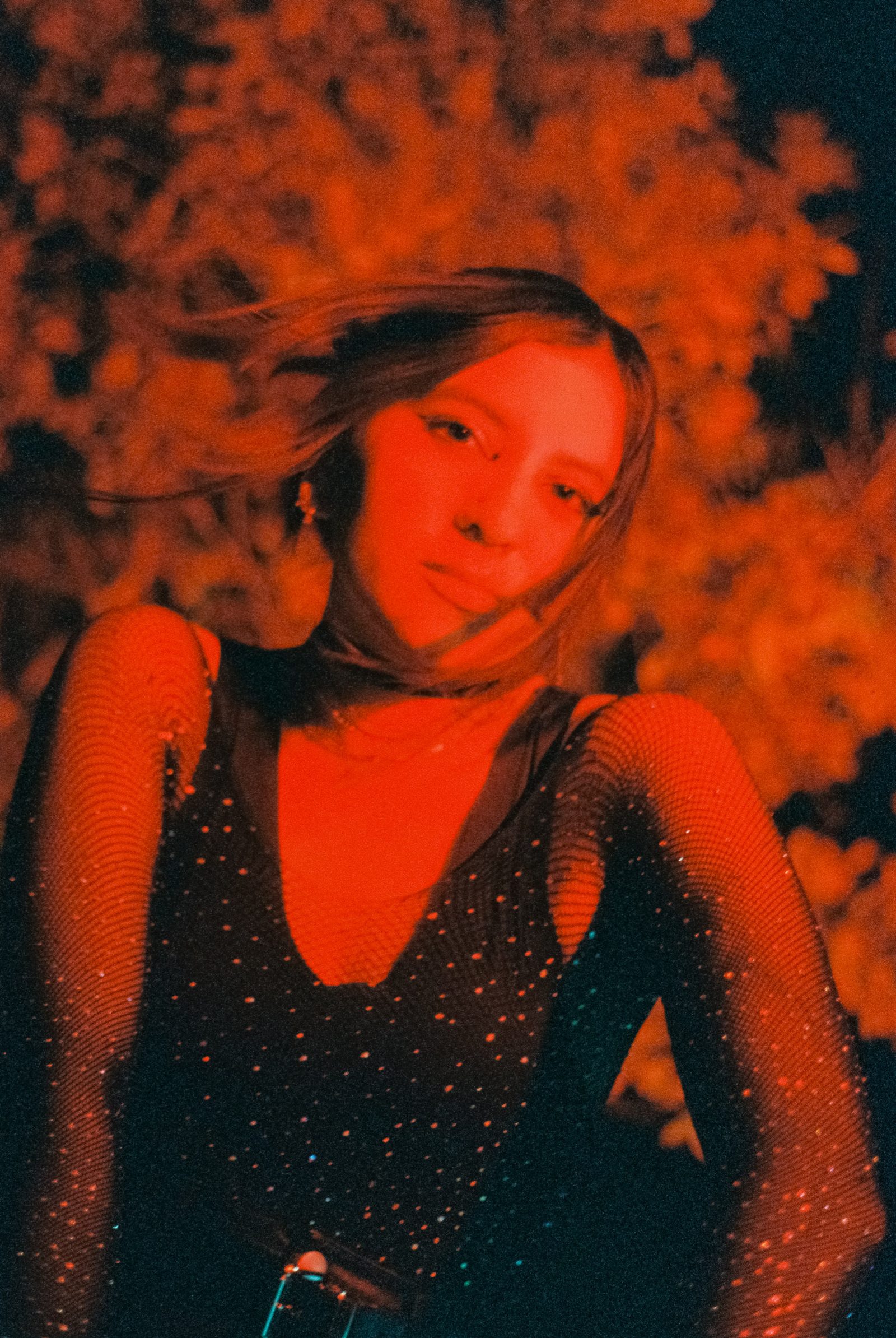 Angela Hernandez in a punk-inspired black outfit under red nighttime light, photographed with a grainy cinematic look outdoors.