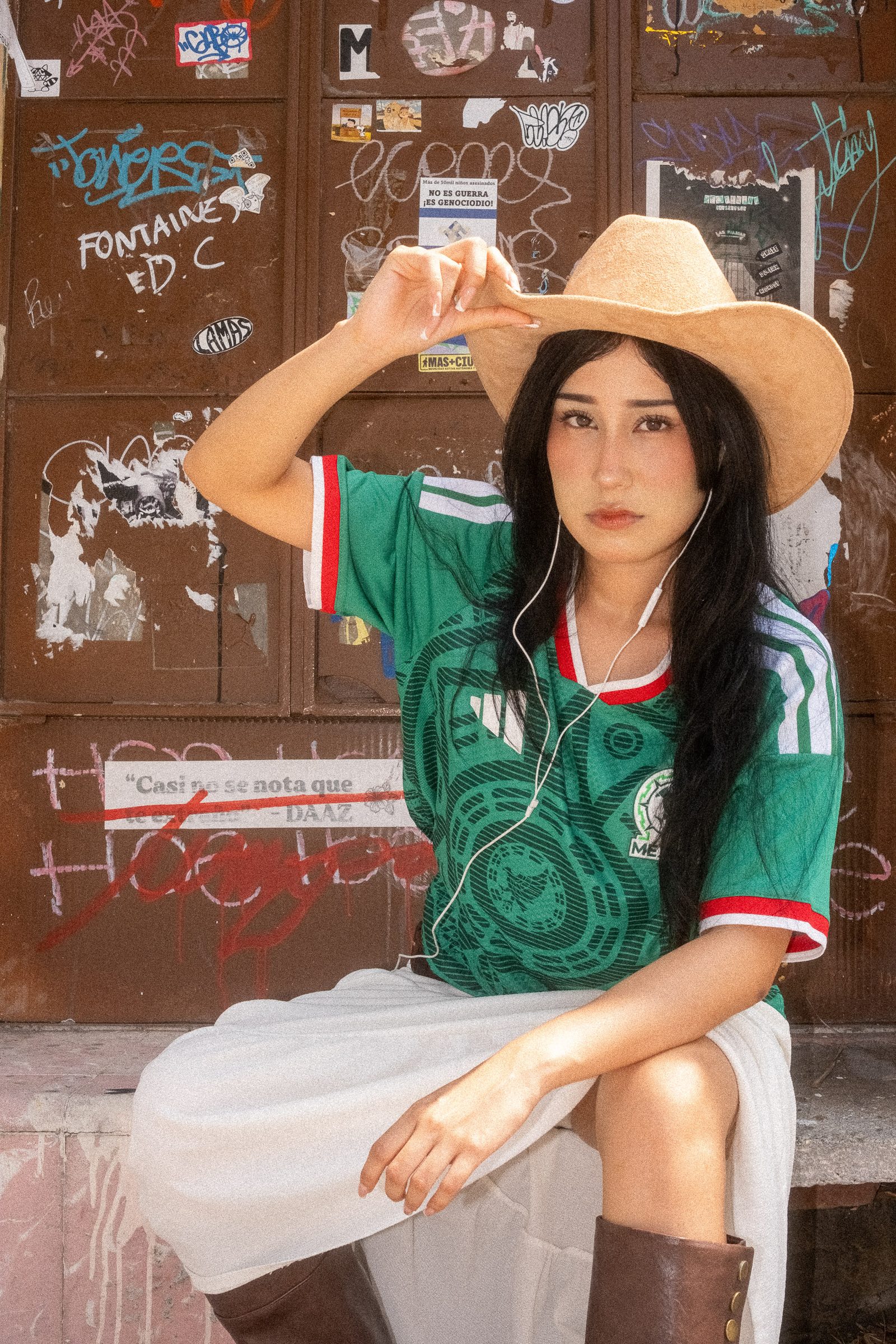 Liz con sombrero y el jersey de la Selección Mexicana sentada en una puerta con graffiti y stickers
