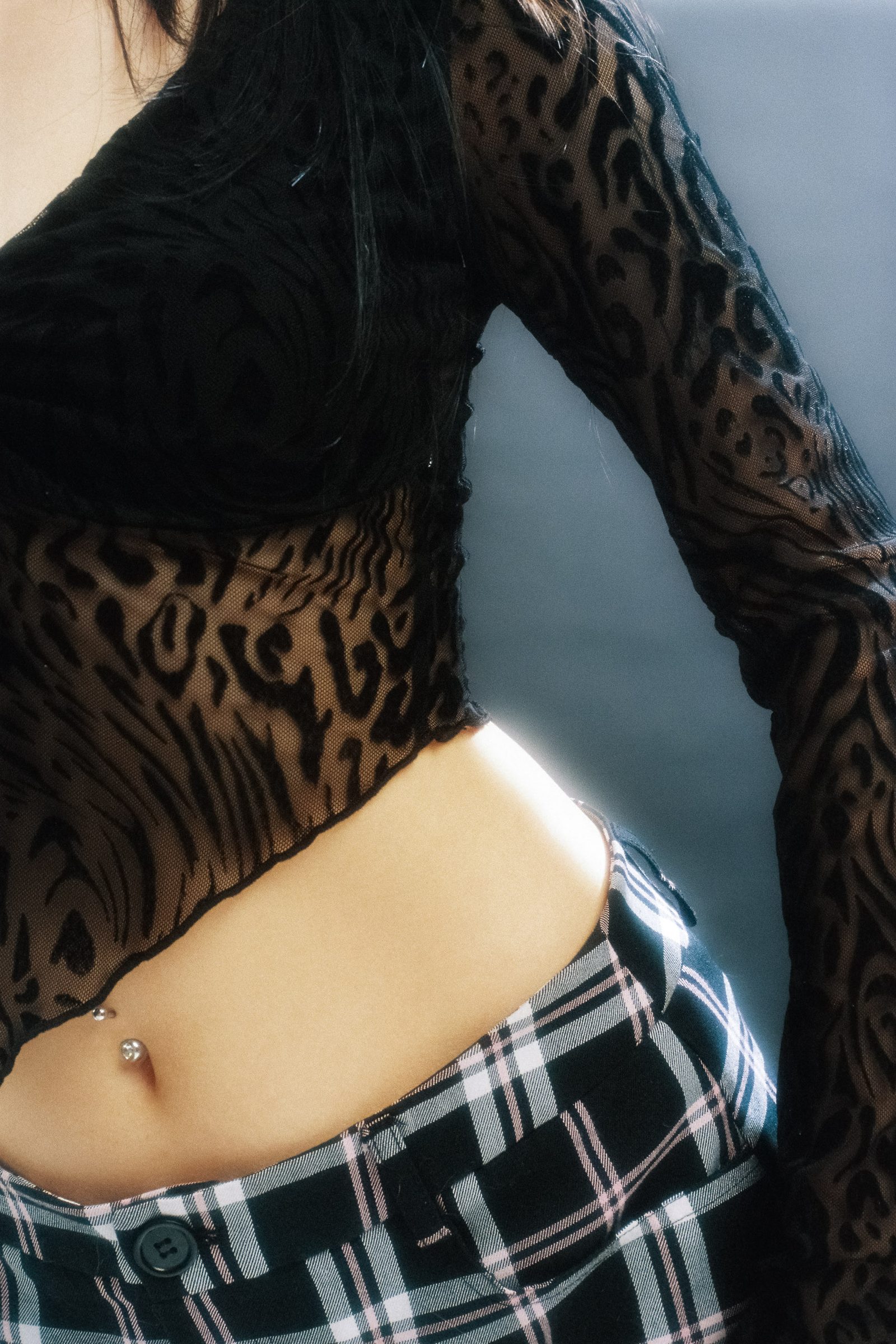 Close-up detail of Dany Mass wearing a black sheer patterned top and plaid skirt, photographed on film with soft side light.