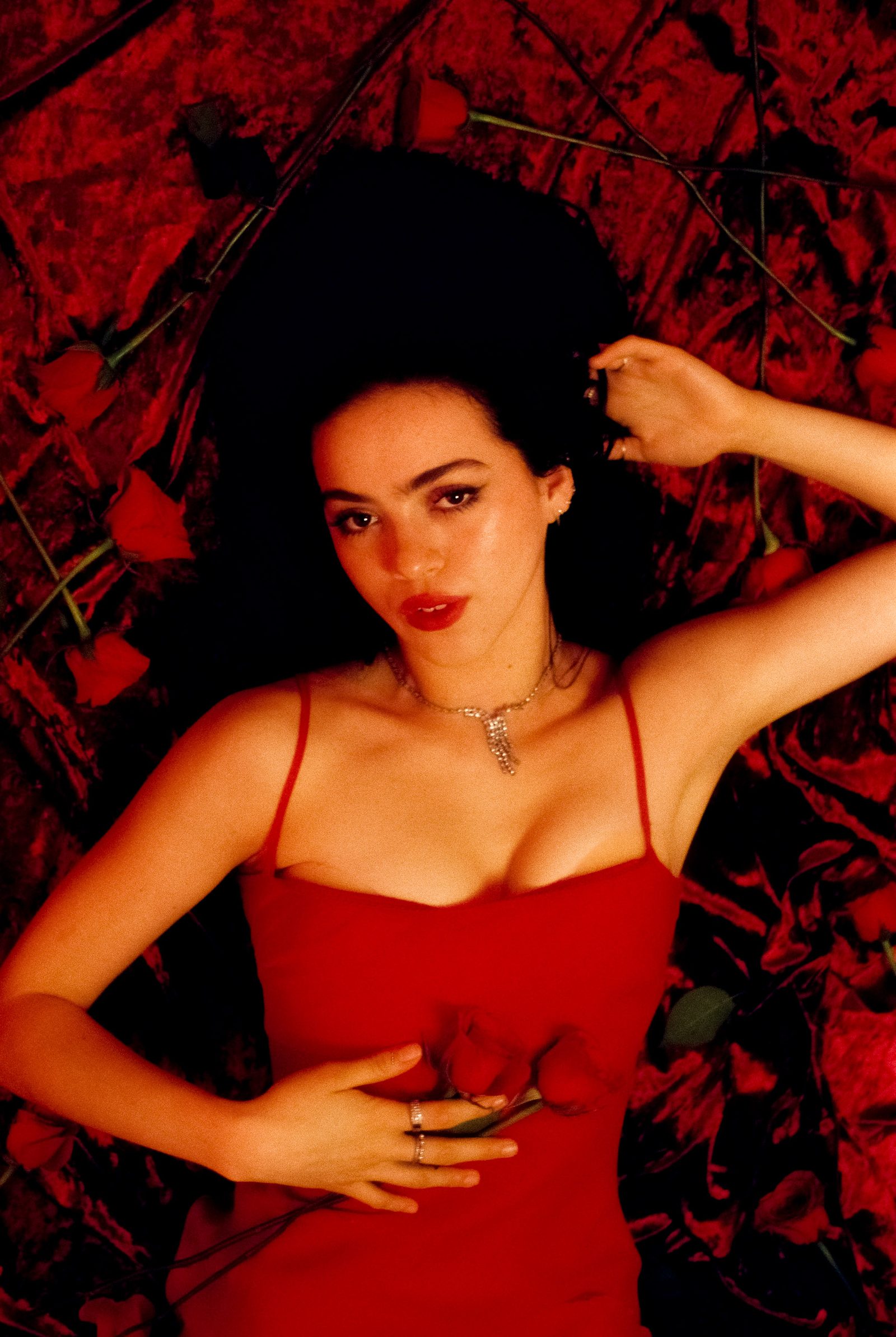 Ale Alvarado in a red dress lying on red velvet with roses, photographed on film in a dramatic studio portrait.