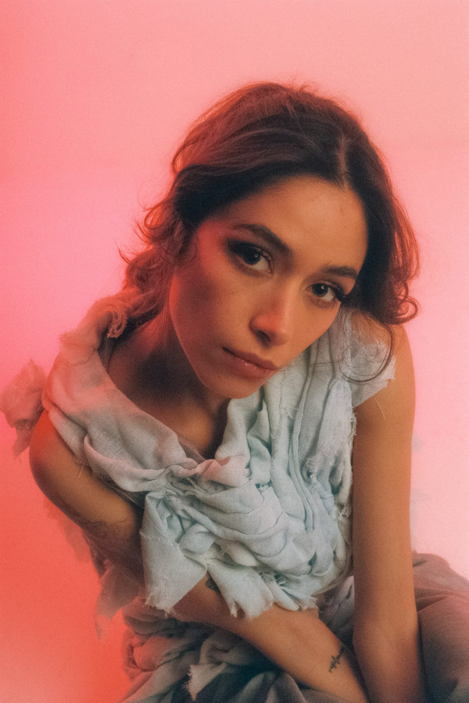 Michelle Malacara leaning forward in a pale textured fabric top, photographed on film with soft pink studio lighting.