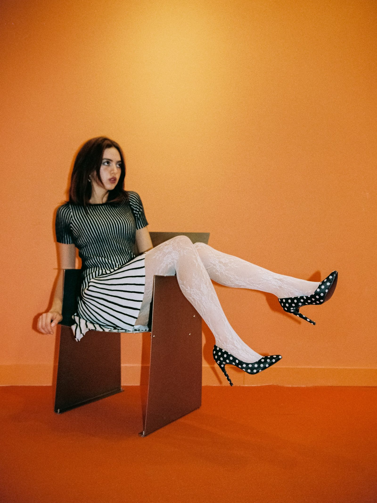 Ale sentada en una silla de acero en un espacio naranja