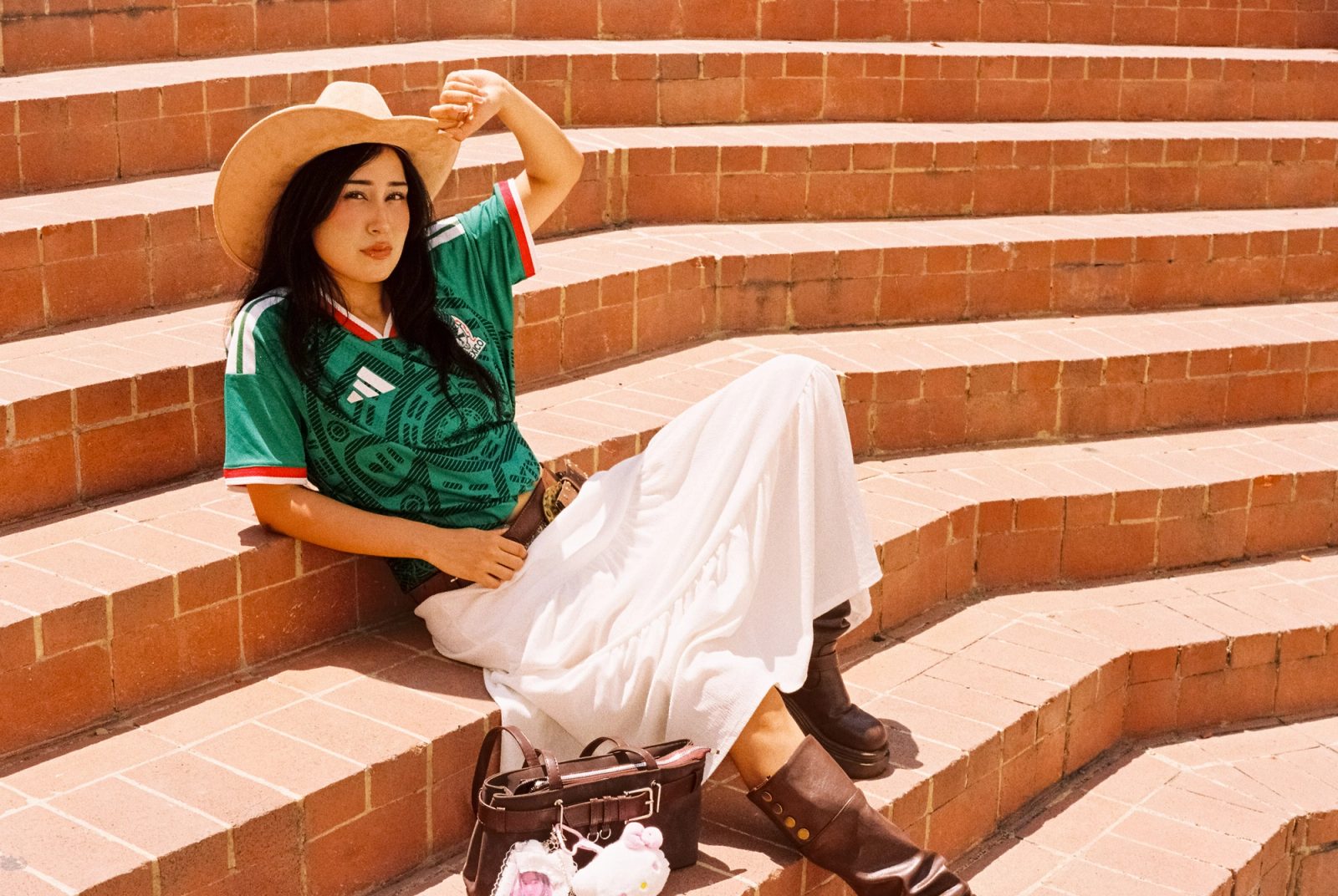 Liz con sombrero y el jersey de la Selección Mexicana recostada en unas escaleras de ladrillo