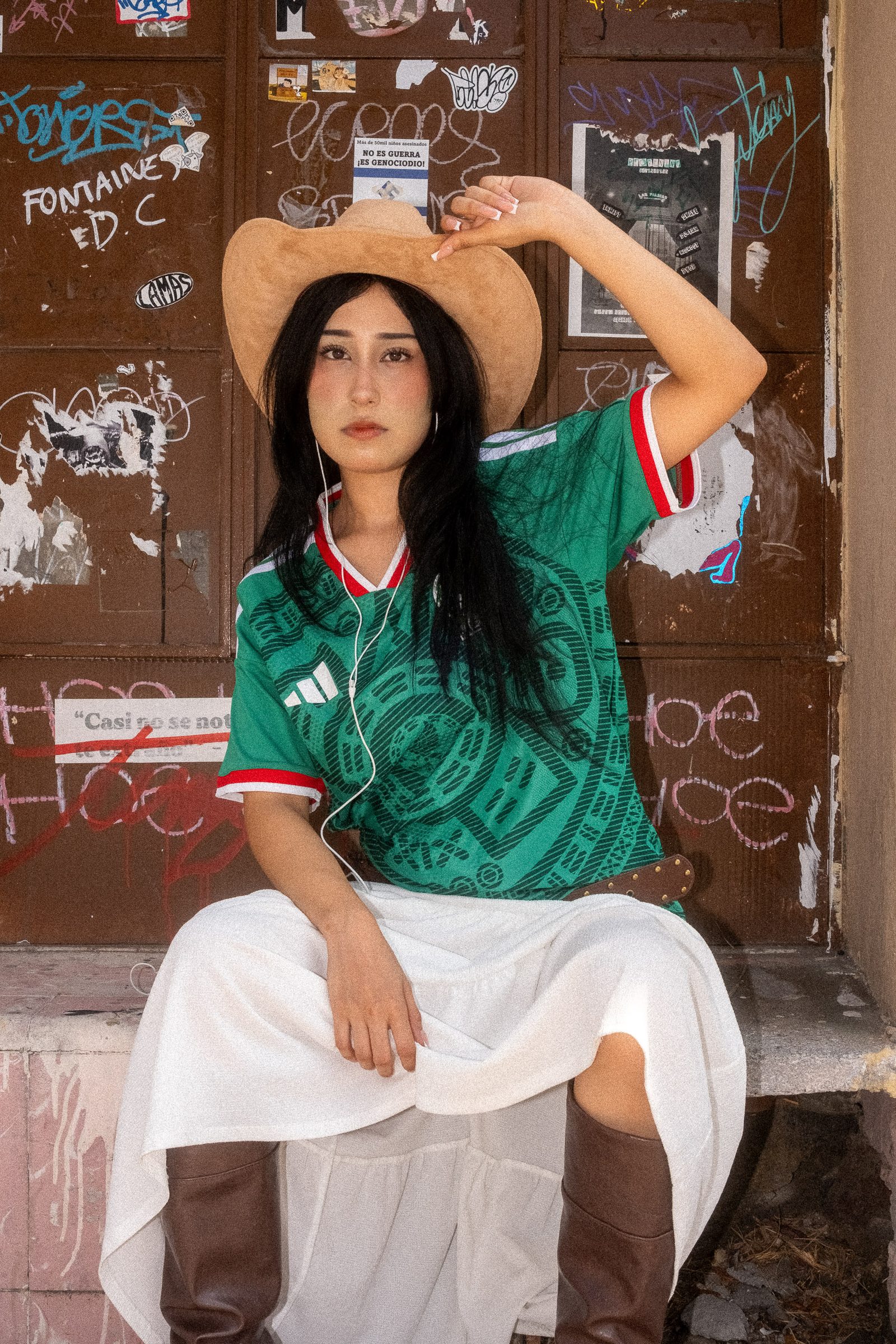 Liz con sombrero y el jersey de la Selección Mexicana sentada en una puerta con graffiti y stickers
