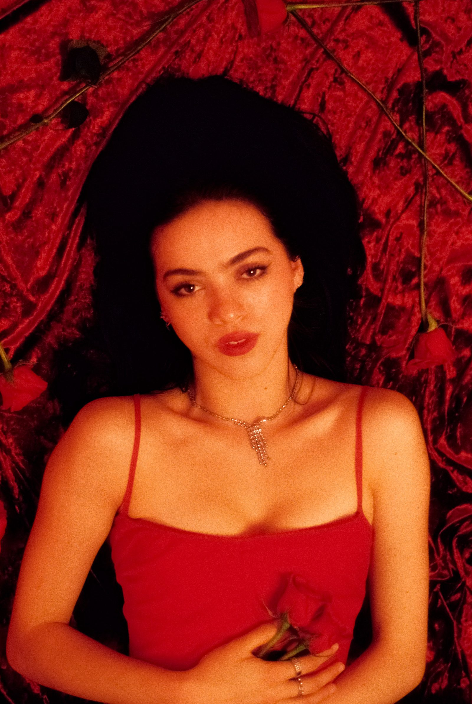 Ale Alvarado lying on red velvet with roses around her, photographed on film in a saturated red studio portrait.