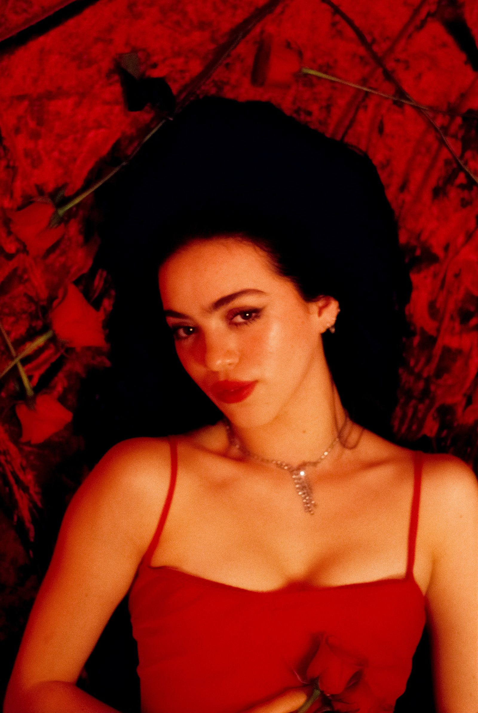 Close-up portrait of Ale Alvarado in a red dress holding roses against red velvet, photographed on film.