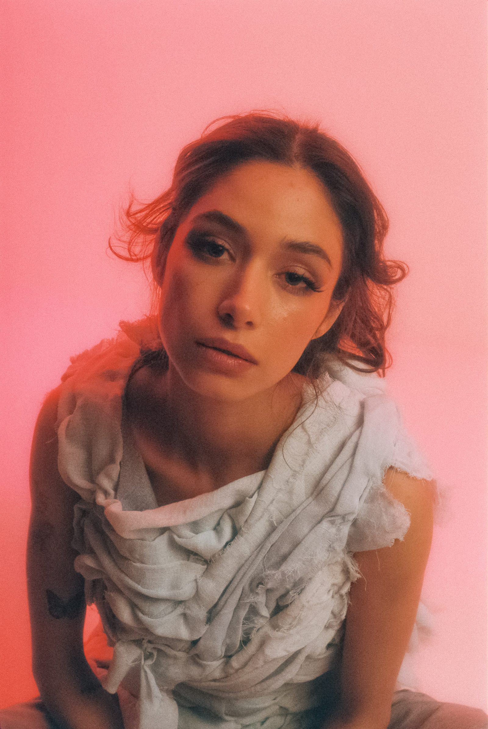 Close-up portrait of Michelle Malacara wearing a sculptural pale fabric top, photographed on film against a pink studio backdrop.