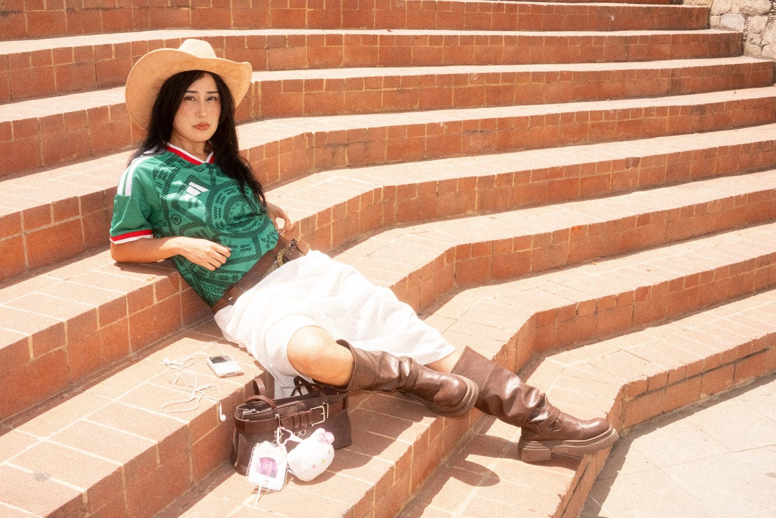Liz con sombrero y el jersey de la Selección Mexicana recostada en unas escaleras de ladrillo