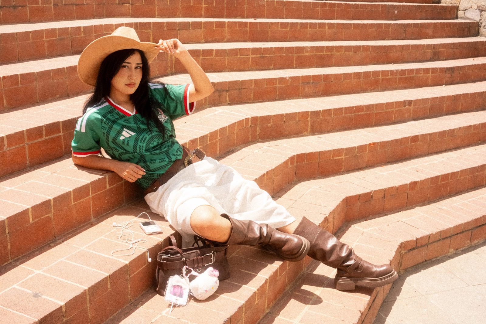 Liz con sombrero y el jersey de la Selección Mexicana recostada en unas escaleras de ladrillo