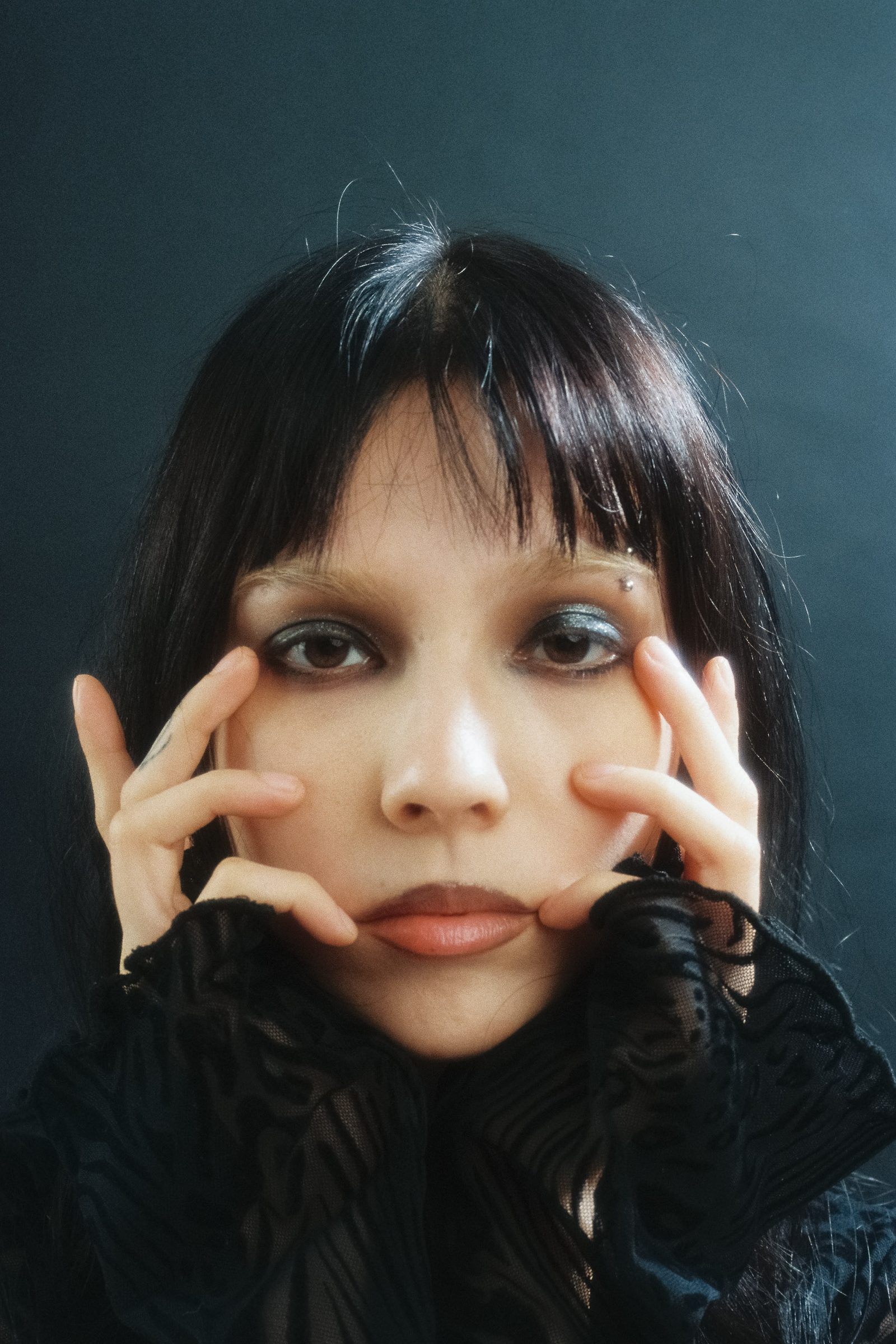 Close-up portrait of Dany Mass with her hands framing her face, photographed on film against a dark studio backdrop.