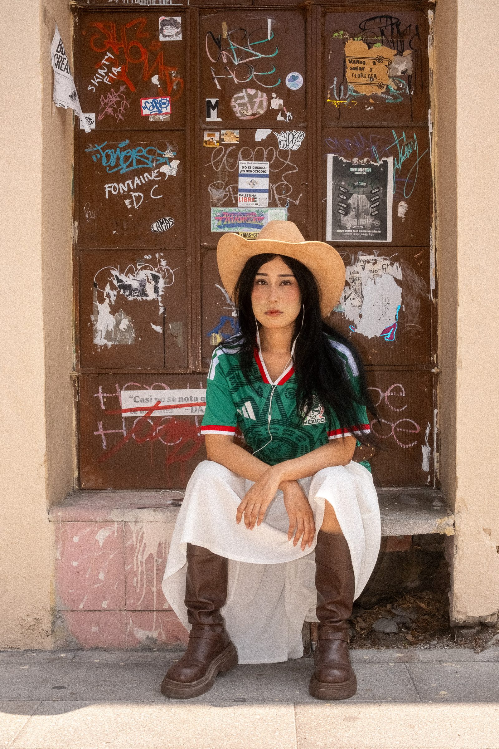 Liz con sombrero y el jersey de la Selección Mexicana sentada en una puerta con graffiti y stickers