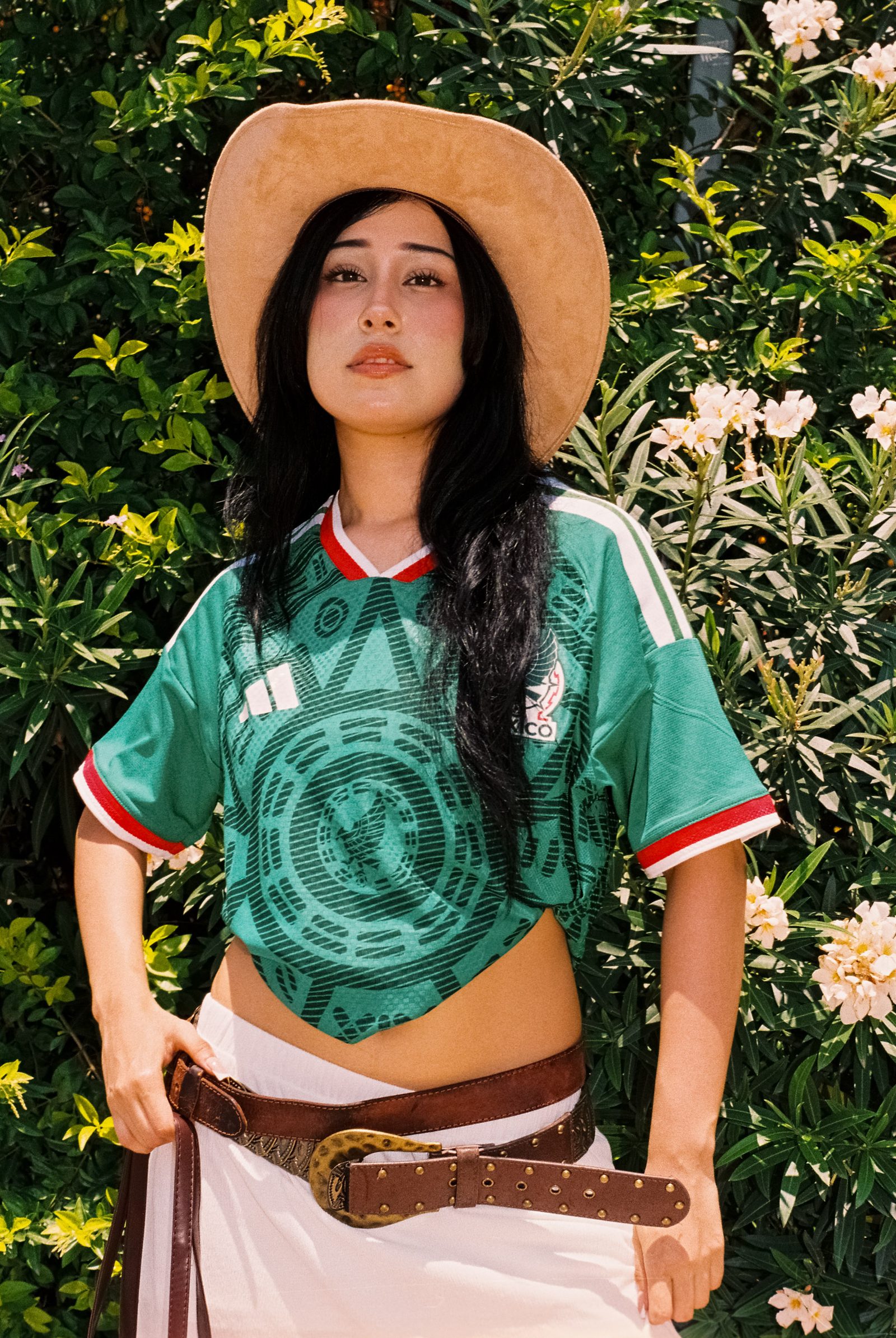 Liz con sombrero y el jersey de la Selección Mexicana en un fondo de hojas verdes