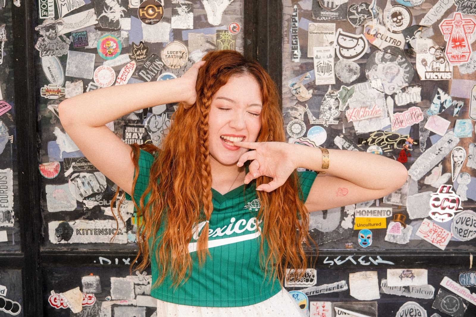 A redhaired girl dressed in Mexico's colors playing with her hair and her fingers in mouth